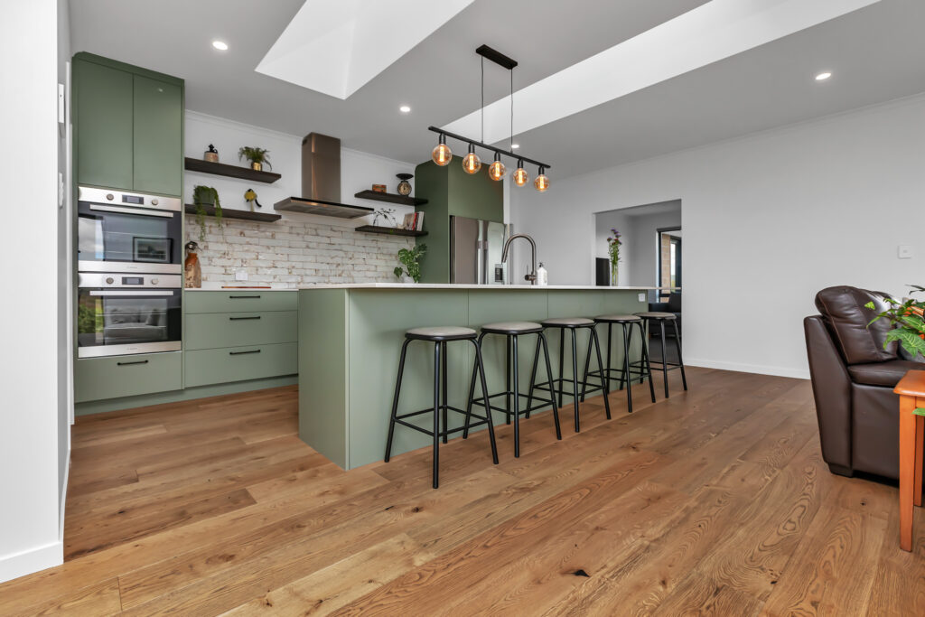 Kitchen featuring gleaming Oak Leather plank flooring, sleek green cabinetry, and accents, all bathed in warm lighting to create a relaxed and inviting atmosphere in this family home.